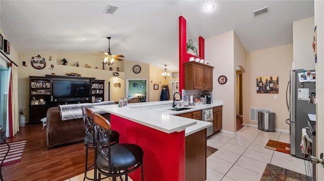 kitchen featuring arched walkways, a breakfast bar area, a peninsula, visible vents, and light countertops