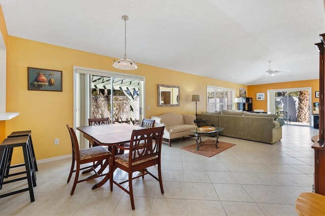 dining space featuring light tile patterned flooring, vaulted ceiling, a textured ceiling, ceiling fan, and baseboards