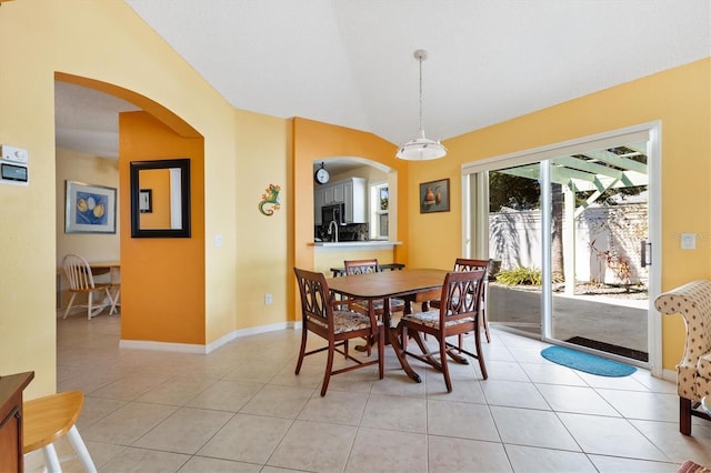 dining area featuring arched walkways, vaulted ceiling, baseboards, and light tile patterned floors