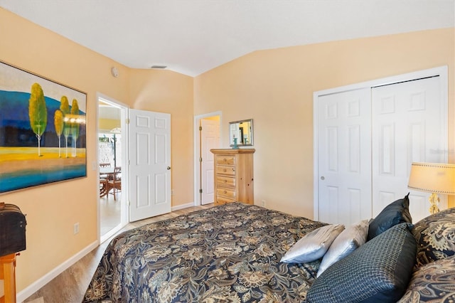 bedroom with wood finished floors, visible vents, baseboards, vaulted ceiling, and a closet