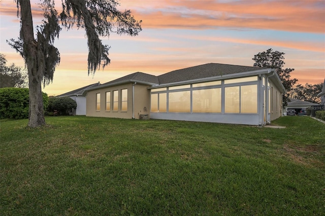 back of house at dusk featuring a yard and stucco siding