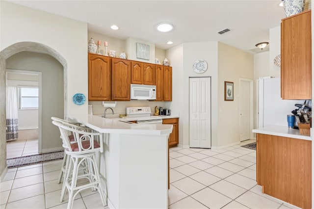 5135 Aurora Dr, Leesburg, FL 34748 - kitchen with light tile patterned floors, a breakfast bar area, a peninsula, white appliances, and visible vents