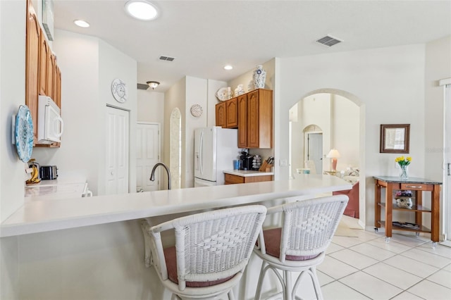 5135 Aurora Dr, Leesburg, FL 34748 - kitchen with white appliances, light tile patterned floors, visible vents, arched walkways, and brown cabinets