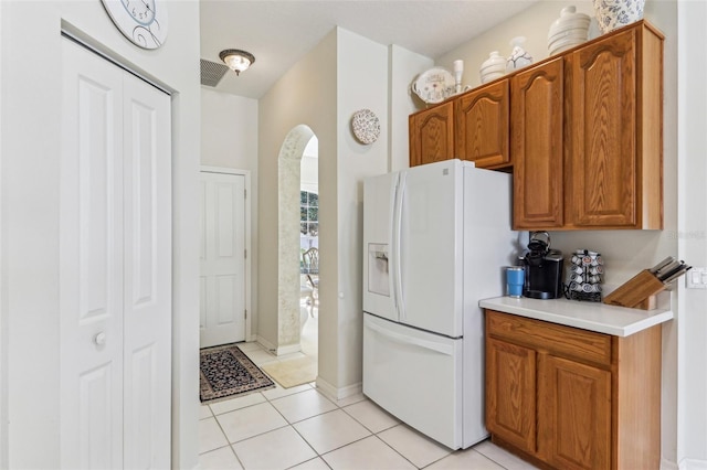 5135 Aurora Dr, Leesburg, FL 34748 - kitchen with arched walkways, light countertops, brown cabinetry, light tile patterned flooring, and white fridge with ice dispenser