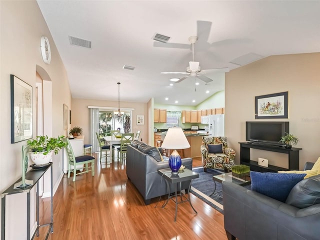 living area with lofted ceiling, light wood finished floors, visible vents, and ceiling fan with notable chandelier