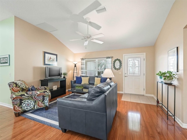 living area featuring lofted ceiling, wood finished floors, visible vents, baseboards, and a ceiling fan