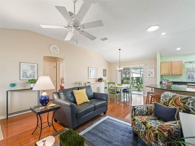 living room with lofted ceiling, visible vents, ceiling fan with notable chandelier, and light wood-style flooring