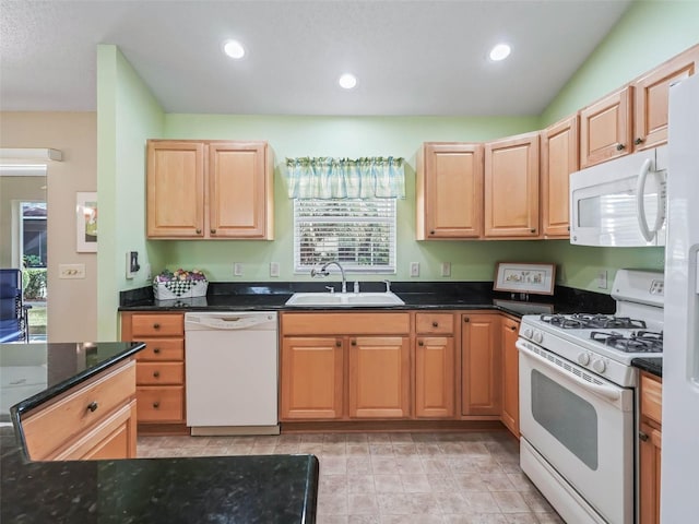 kitchen featuring light brown cabinets, recessed lighting, white appliances, a sink, and dark stone counters