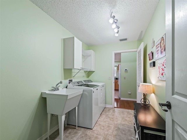 clothes washing area featuring visible vents, cabinet space, washing machine and dryer, a textured ceiling, and baseboards