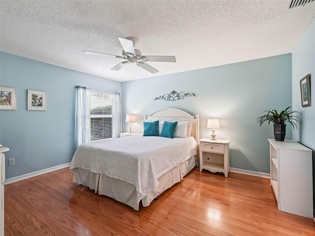 bedroom with light wood finished floors, a textured ceiling, baseboards, and a ceiling fan