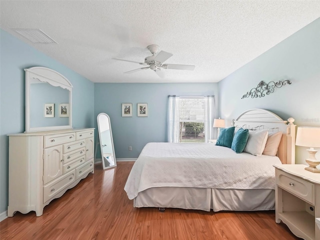 bedroom with baseboards, visible vents, a ceiling fan, wood finished floors, and a textured ceiling