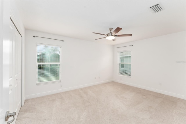 empty room featuring baseboards, a ceiling fan, visible vents, and light colored carpet