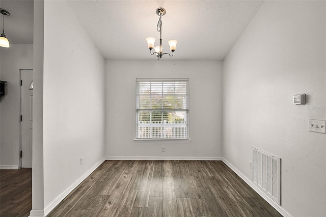 unfurnished dining area with a notable chandelier, dark hardwood / wood-style floors, and a textured ceiling