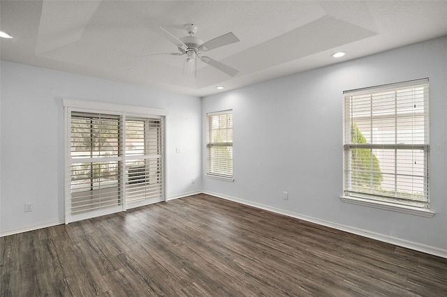 unfurnished room featuring a raised ceiling, ceiling fan, and dark wood-type flooring