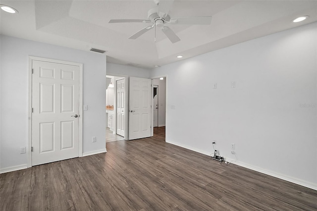 unfurnished bedroom with a raised ceiling, ceiling fan, ensuite bath, and dark wood-type flooring