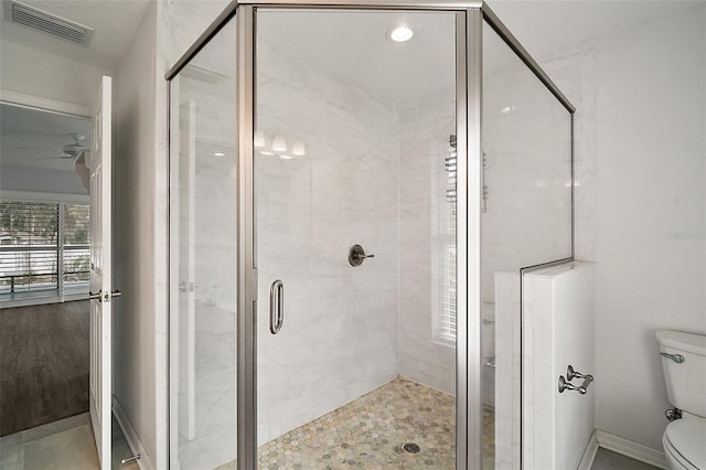 bathroom with ceiling fan, a shower with shower door, and toilet