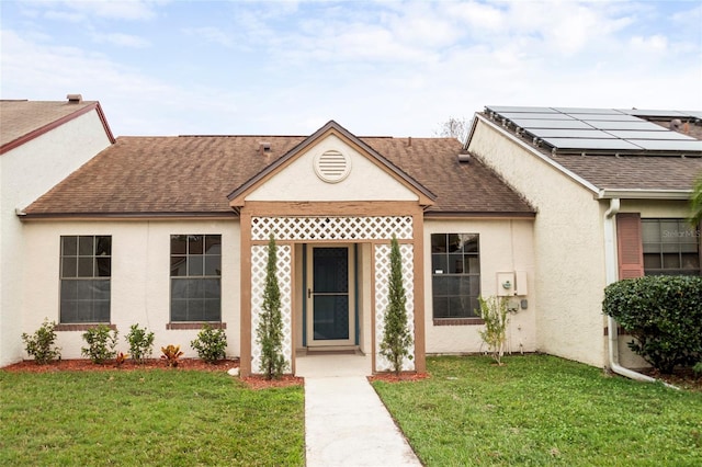 view of front of house with stucco siding, a front lawn, and roof with shingles