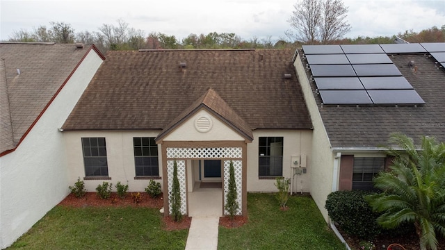 view of front facade with a shingled roof, a front yard, roof mounted solar panels, and stucco siding