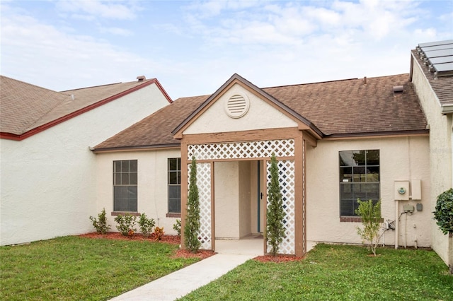 view of front of house with roof with shingles, a front lawn, and stucco siding