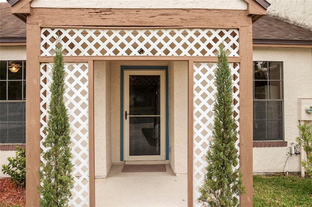 property entrance featuring a shingled roof and stucco siding