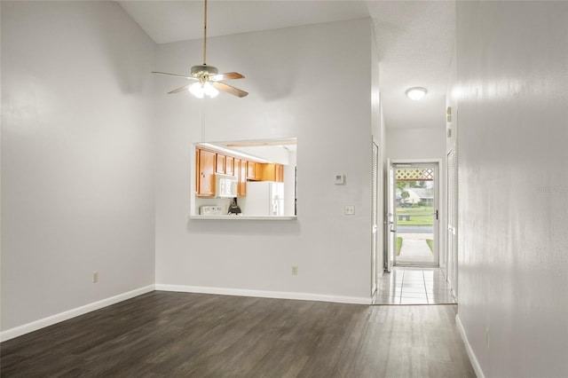 unfurnished living room featuring a ceiling fan, a high ceiling, baseboards, and dark wood-style flooring