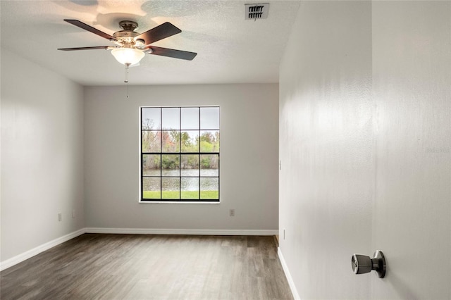 empty room featuring a textured ceiling, ceiling fan, visible vents, baseboards, and dark wood finished floors