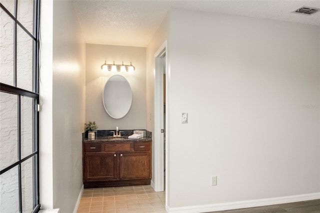 bathroom with visible vents, baseboards, a textured ceiling, and vanity