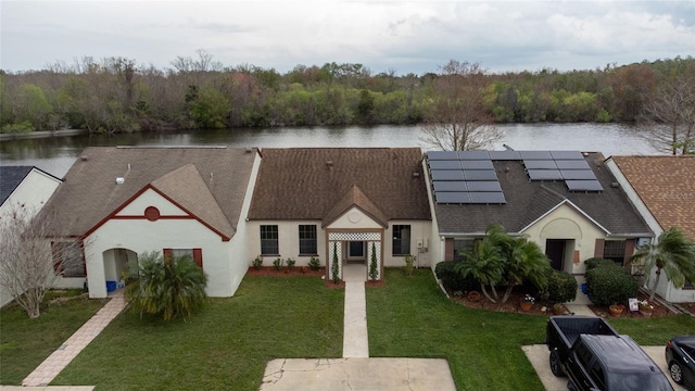 view of front of home featuring solar panels, a shingled roof, a water view, a front yard, and a view of trees