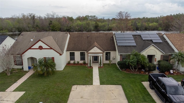 view of front facade featuring a front yard, a shingled roof, roof mounted solar panels, a wooded view, and stucco siding