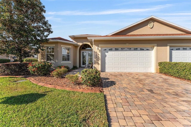 single story home with a garage, french doors, decorative driveway, stucco siding, and a front lawn