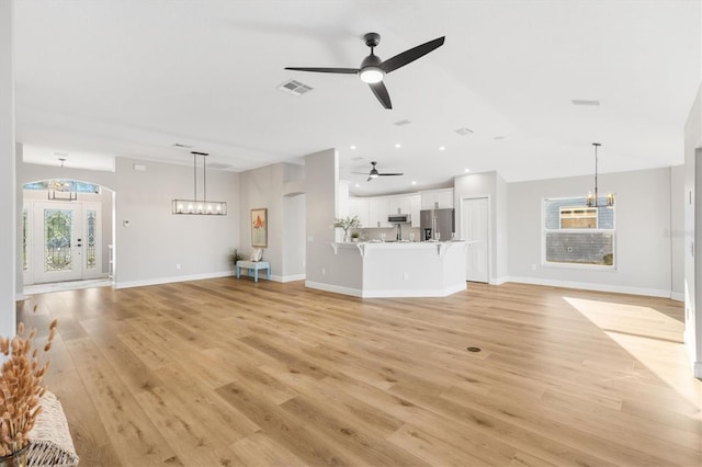 unfurnished living room featuring ceiling fan with notable chandelier and light wood-type flooring