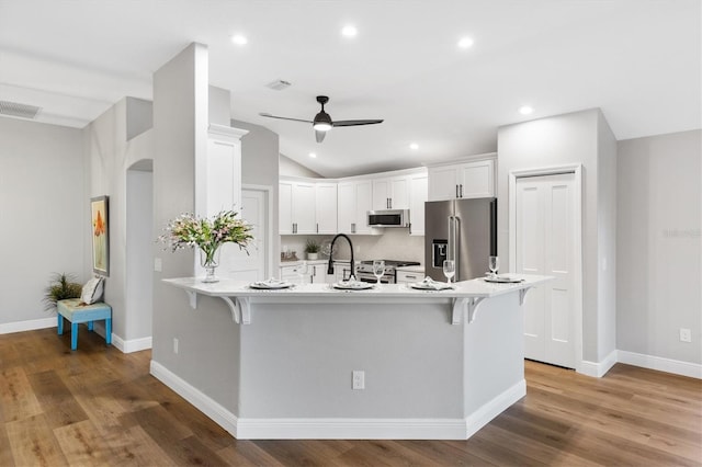 kitchen featuring white cabinetry, kitchen peninsula, lofted ceiling, appliances with stainless steel finishes, and a kitchen bar