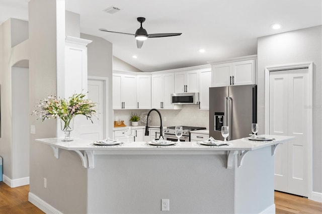 kitchen featuring white cabinetry, appliances with stainless steel finishes, a kitchen bar, and light wood-type flooring