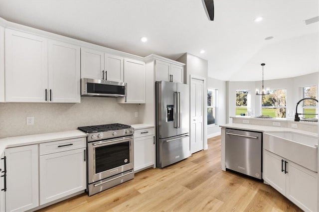 kitchen featuring hanging light fixtures, stainless steel appliances, white cabinets, decorative backsplash, and light wood-type flooring