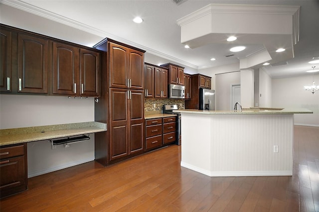 kitchen with dark brown cabinetry, ornamental molding, appliances with stainless steel finishes, built in study area, and dark wood finished floors