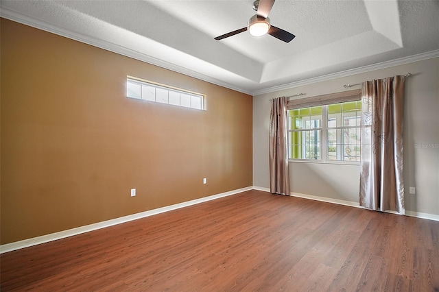 empty room with a ceiling fan, baseboards, a raised ceiling, and wood finished floors