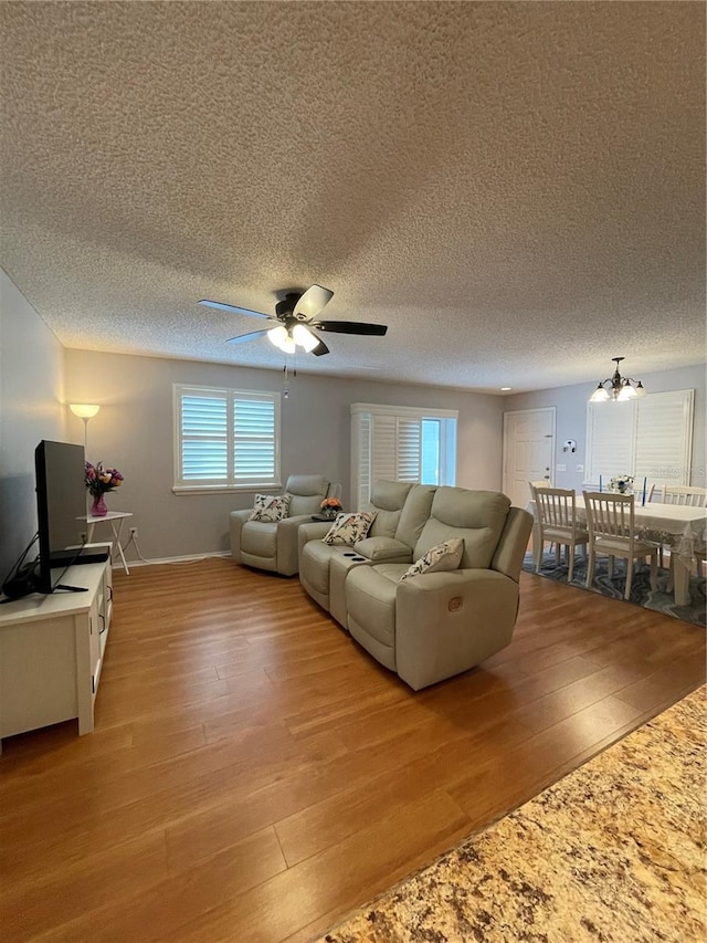 living room with ceiling fan with notable chandelier, light hardwood / wood-style flooring, and a textured ceiling