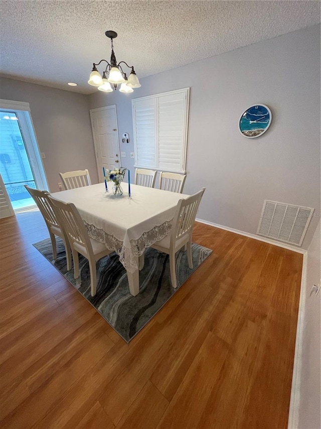 dining room featuring a textured ceiling, hardwood / wood-style floors, and an inviting chandelier