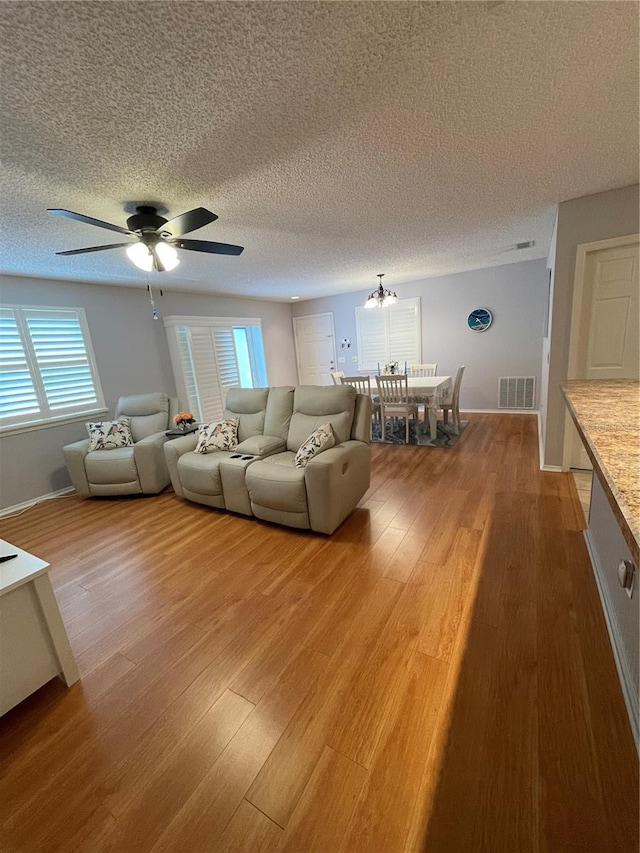 unfurnished living room featuring hardwood / wood-style flooring, a textured ceiling, and ceiling fan with notable chandelier