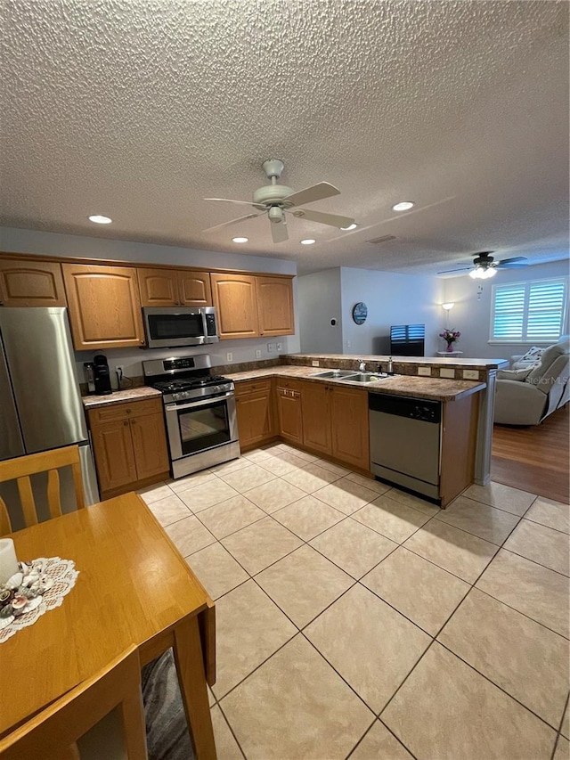 kitchen featuring appliances with stainless steel finishes, sink, light tile patterned floors, ceiling fan, and kitchen peninsula