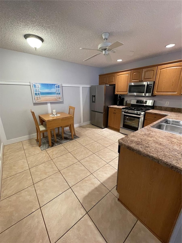 kitchen with appliances with stainless steel finishes, sink, light tile patterned flooring, a textured ceiling, and ceiling fan