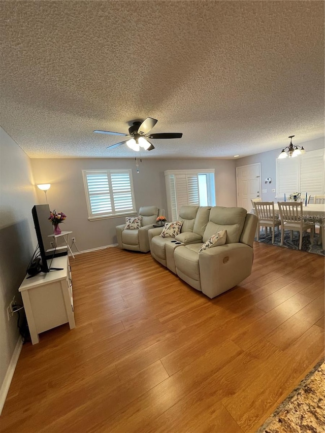 living room featuring ceiling fan with notable chandelier, light wood-type flooring, and a textured ceiling