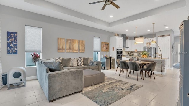 living area featuring light tile patterned floors, recessed lighting, a ceiling fan, baseboards, and a tray ceiling