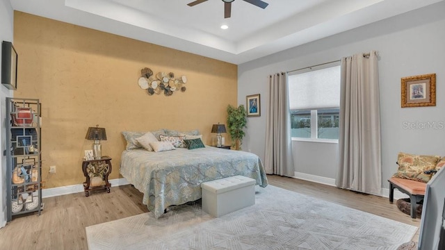 bedroom with recessed lighting, a raised ceiling, light wood-style flooring, and baseboards