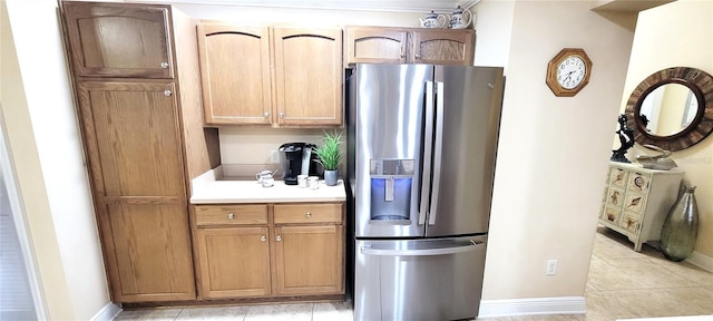 kitchen featuring light countertops, stainless steel refrigerator with ice dispenser, baseboards, and light tile patterned floors