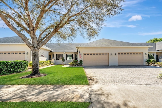 ranch-style house with a front lawn, decorative driveway, an attached garage, and stucco siding