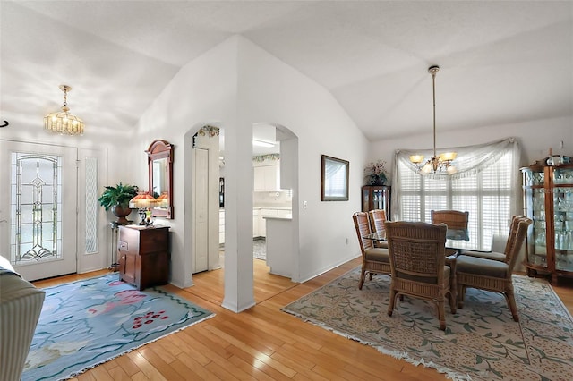 dining area with a chandelier, high vaulted ceiling, arched walkways, and light wood-style flooring