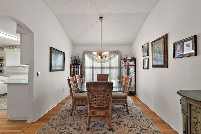 dining space featuring vaulted ceiling, an inviting chandelier, arched walkways, and light wood-style floors