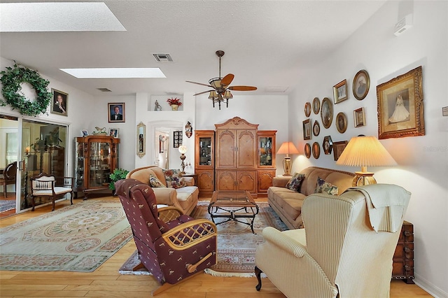 living room with light wood-style floors, a skylight, visible vents, and a ceiling fan