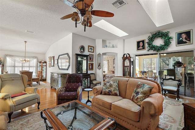 living room with light wood-style floors, vaulted ceiling with skylight, a healthy amount of sunlight, and visible vents